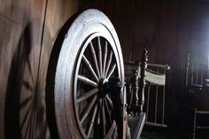 an old wooden wagon wheel sitting next to a rocking chair in a room with dark wood walls