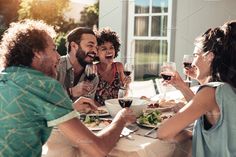 a group of people sitting around a table eating and drinking wine