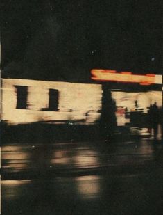 a blurry photo of a gas station at night with the lights on and people walking by