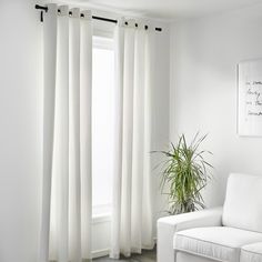 a white couch sitting next to a window with curtains on it's sides and a potted plant in front of the window