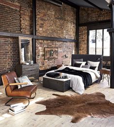 a bedroom with exposed brick walls and wooden flooring is pictured in this image, the bed has a black blanket on it