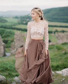 a woman standing on top of a lush green hillside wearing a brown skirt and crop top