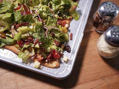 a salad with lettuce, tomatoes and other vegetables on a tray next to salt and pepper shakers