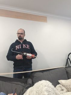 a man standing in front of a mirror holding a paintbrush and brush with another person sitting on the couch behind him