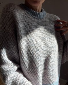 a woman wearing a white sweater and holding her hand on her shoulder while standing in front of a window