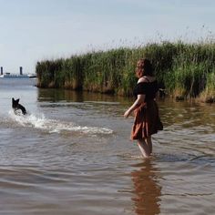 a woman and her dog are wading in the water near some tall grass,