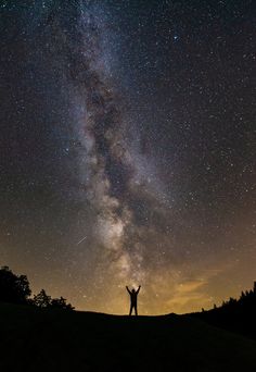 a man standing on top of a hill under a night sky filled with lots of stars