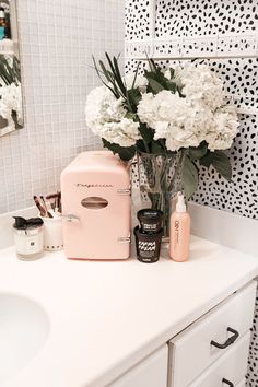 a pink refrigerator sitting on top of a white counter next to a vase filled with flowers