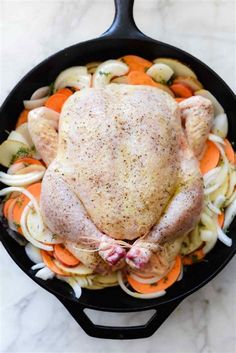 a whole chicken in a cast iron skillet with carrots and onions on the side