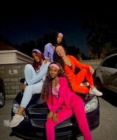 four young women sitting on the hood of a car in front of a house at night