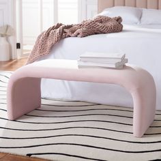 a pink bench sitting on top of a white rug next to a neatly made bed