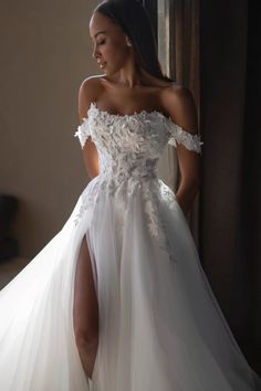 a woman in a white wedding dress standing next to a window with her leg up