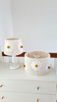 two white lamps sitting on top of a dresser next to a lamp shade with daisies