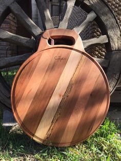 a wooden cutting board sitting on the ground next to an old wagon wheel and grass