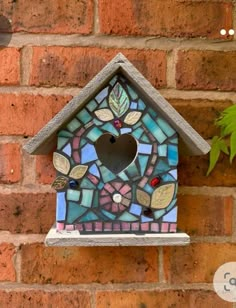 a birdhouse made out of stained glass and stone with leaves on the top, hanging from a brick wall