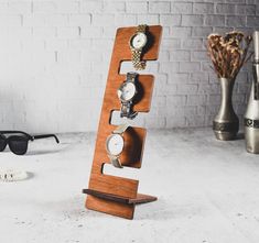 a wooden stand with four watches on it and sunglasses in the back ground next to a brick wall