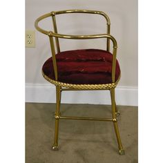 a chair with a red velvet seat and gold metal frame, against a white wall