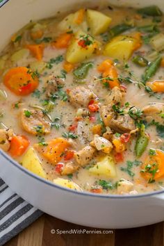 a white pot filled with chicken, potatoes and carrots on top of a wooden table