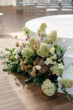 flowers and greenery are arranged on the floor next to a round table with chairs in the background