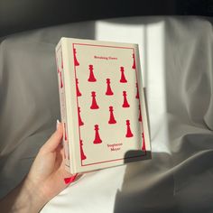 a person holding up a book with red chess pieces on it