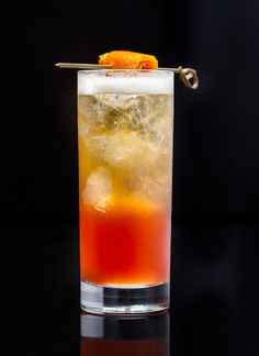 a tall glass filled with ice and an orange slice on the rim, sitting on a black surface