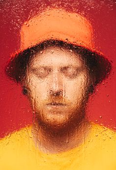 a man's face is shown through the rain on a red and yellow background