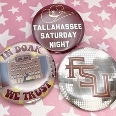 three badges with words on them sitting on a pink background and white stars in the foreground