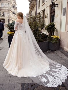 a woman in a wedding dress is walking down the street with her veil over her shoulder