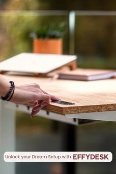 a person holding a cell phone on top of a wooden table next to a plant