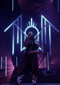 a man standing on top of a stage in front of purple lights and holding a microphone