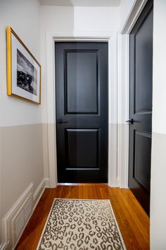 a black door in a white room next to a rug