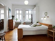 a bed room with a neatly made bed next to two windows and a wooden floor