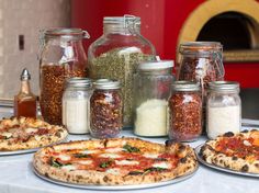 several pizzas and spices on a table