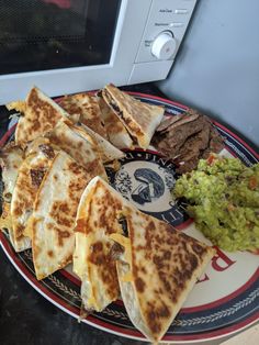 some quesadillas and guacamole on a plate in front of a microwave