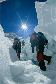 three climbers climbing up the side of a snow covered mountain with bright sun in background