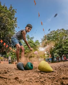 a young boy kicking around balls in the dirt