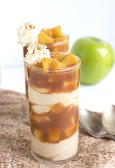 two desserts with apples and whipped cream in them sitting on a table next to spoons