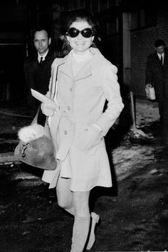 a black and white photo of a woman in a trench coat walking down the street