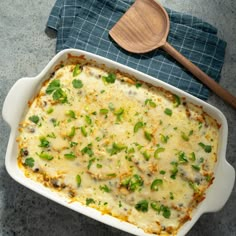 a casserole dish with cheese and green onions in it next to a wooden spoon