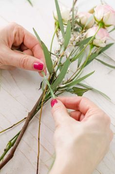 two hands are working on the stems of an eucalyptus plant with pink and white flowers