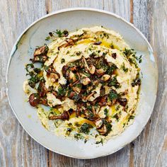 a white plate topped with hummus and mushrooms on top of a wooden table next to a fork