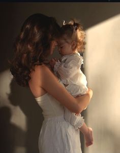 a woman holding a small child in her arms while she is wearing a white dress