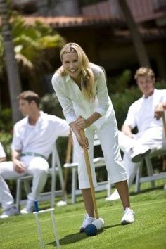 a woman is playing croquet on the lawn with other people in the background