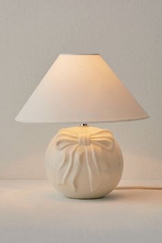 a white table lamp with a light shade on it