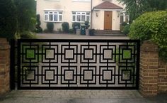 an iron gate in front of a house with trees and bushes around it on a brick driveway