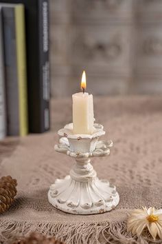 a white candle is sitting on top of a table next to some pine cones and books