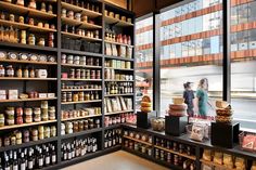 two people are walking through a store with shelves full of food