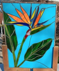 a stained glass painting of a bird of paradise on a wooden easel in front of a brick building