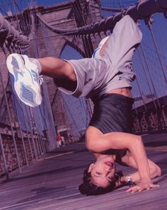 a man doing a handstand on top of a skateboard in front of a bridge