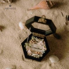 an open jewelry box sitting on the sand with shells and seashells around it